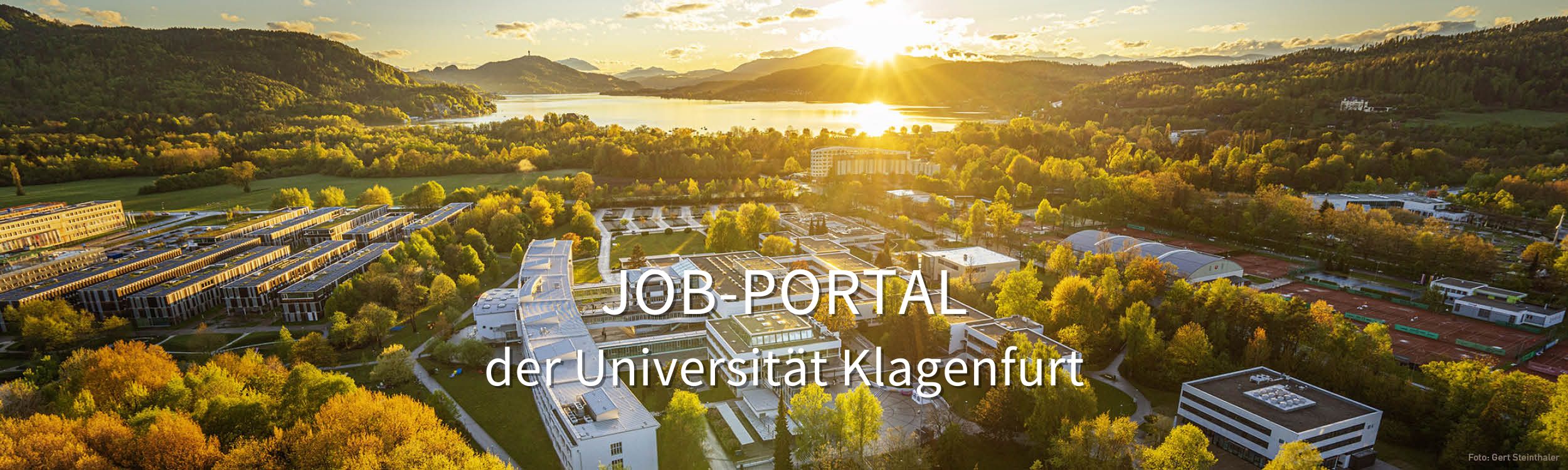 Header des Job-Portals der Universität Klagenfurt: Das Hintergrundfoto zeigt das Gelände der Universität, im Hintergrund der Wörthersee.